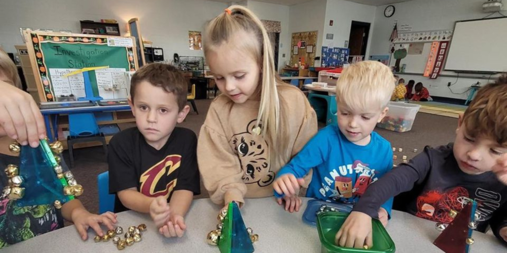 four preschoolers attaching jingle bells to plastic Christmas trees
