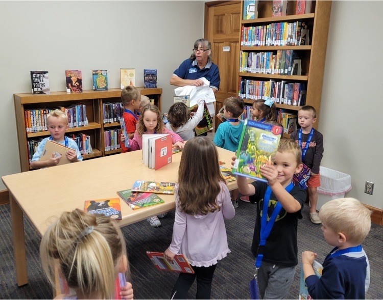 Preschool students looking at books at the library with a Librarian.
