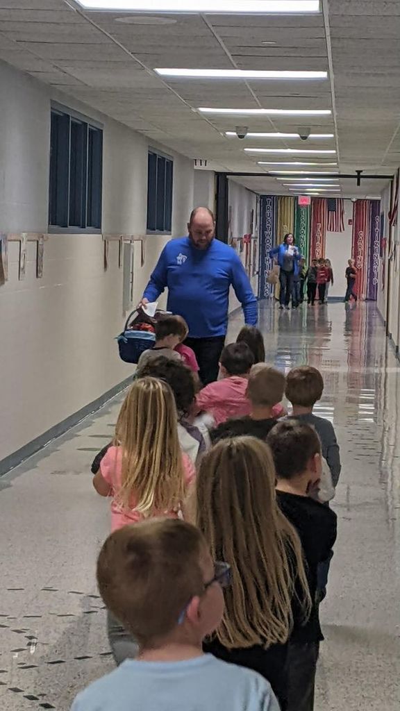 superintendent Will Snyder walking past a line of kindergarten students with a large basket